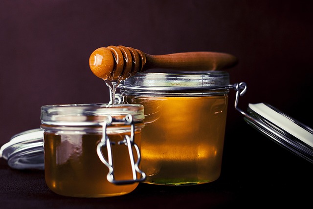 A glass jar of golden honey with a wooden dipper, representing proper storage.