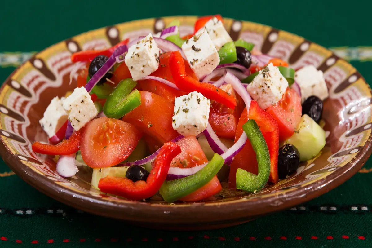 A Greek salad with cubes of feta cheese, tomatoes, peppers, red onion and black olives in a painted clay bowl