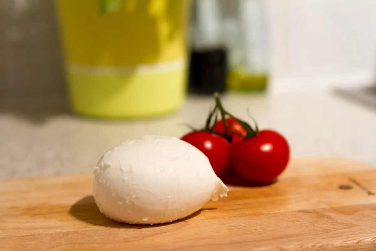 A ball of fresh white mozzarella next to a vine of cherry tomatoes on a wooden cutting board